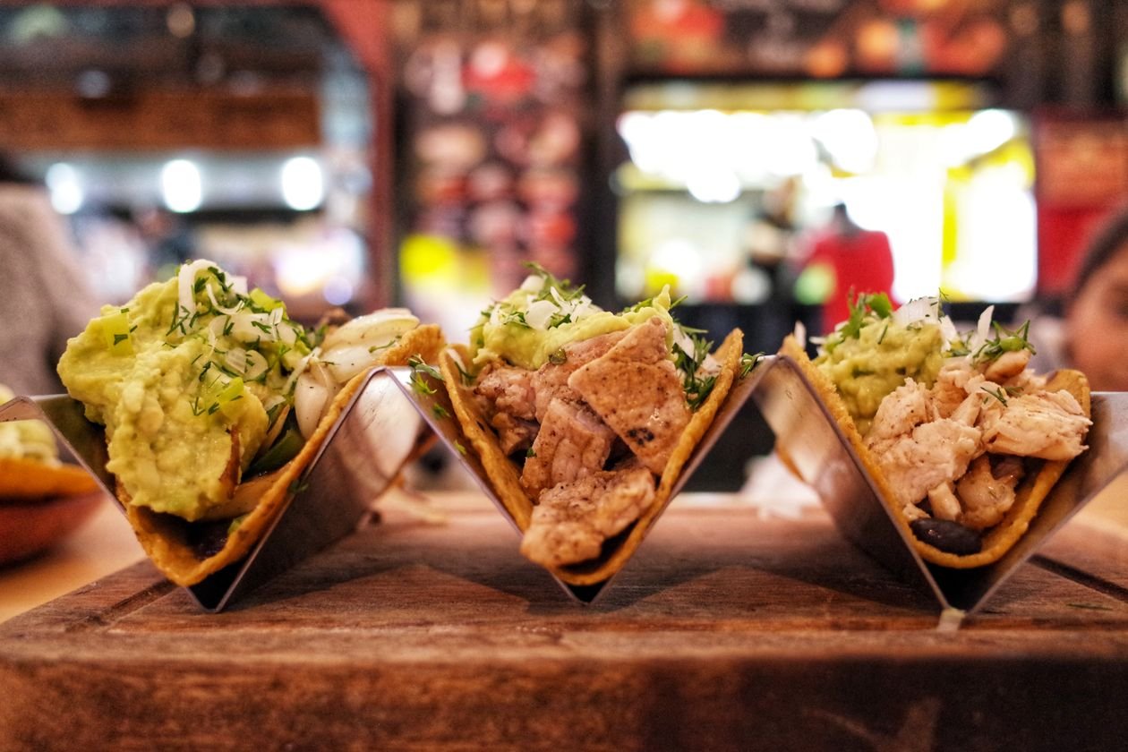 Chicken tacos topped with guacamole, herbs and onions on a restaurant table